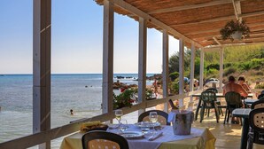 Een restaurant aan zee met gedekte tafels, met uitzicht op het strand en de zee.