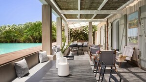 Een overdekt terras met uitzicht op het zwembad, met een tafel, stoelen, een bank en een schilderij aan de muur.