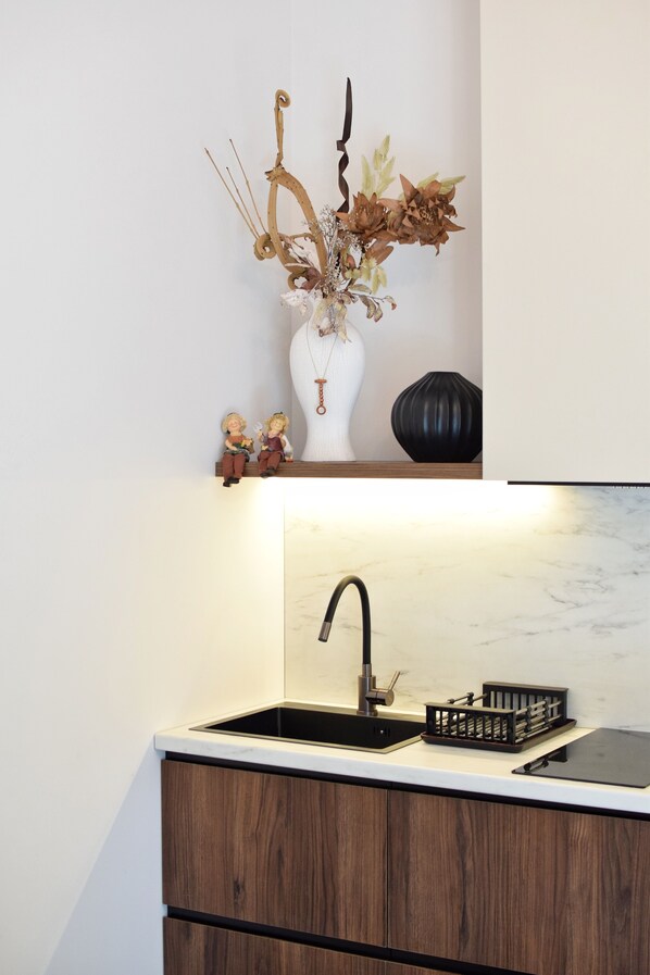 A kitchen with a white countertop, a black sink, and wooden cabinets. - DiAngelo Guesthouse (Yerevan)