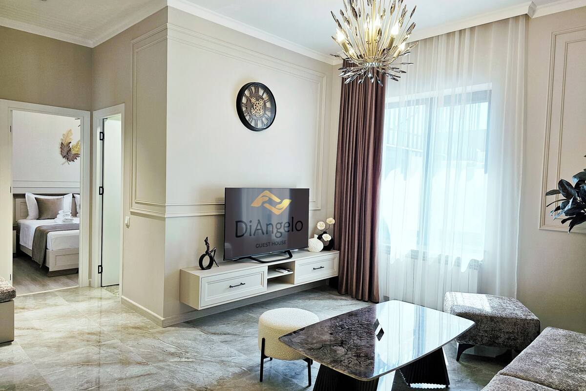A modern hotel room with a dining area, a television, and a decorative clock on the wall.