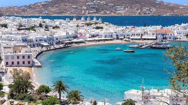 A coastal town with white buildings, a sandy beach, and boats in the water.