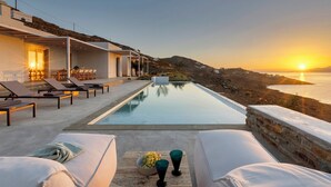 A modern outdoor pool area with lounge chairs and a view of the sunset over the sea.