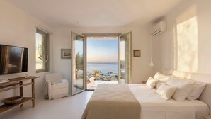 A bedroom with a large bed, a television, and a view of the sea.