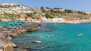 A coastal town with a rocky shoreline, clear blue waters, and a variety of colorful umbrellas and boats.
