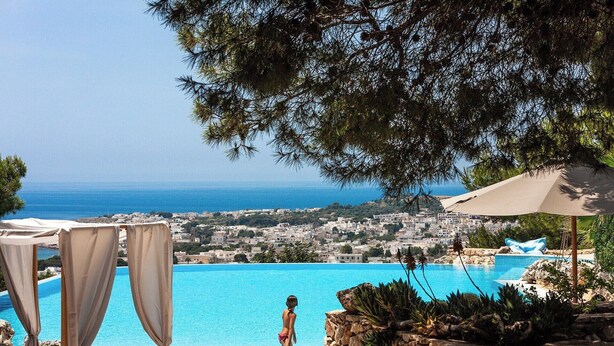 A pool with a clear view of the sea and a town in the background.