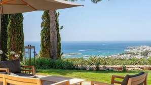 A patio with wooden furniture and a view of the sea and town.