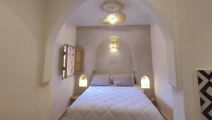 A bedroom with a high arched ceiling, a bed with a white quilted bedspread, two bedside lamps, and a small window. - Riad Marrakech Médina renovated, 5 air-conditioned rooms, with swimming pool (MARRAKECH)