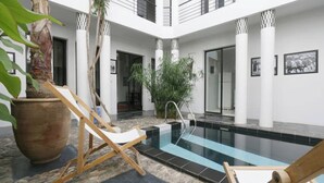 A modern indoor swimming pool with a clear glass bottom, surrounded by white pillars and a wooden deck with lounge chairs. - Riad Marrakech Médina renovated, 5 air-conditioned rooms, with swimming pool (MARRAKECH)
