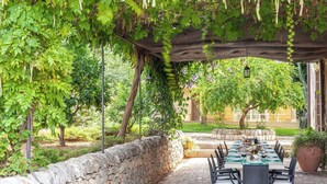 An outdoor dining area with a stone wall, a pergola with vines, and a table set for a meal.