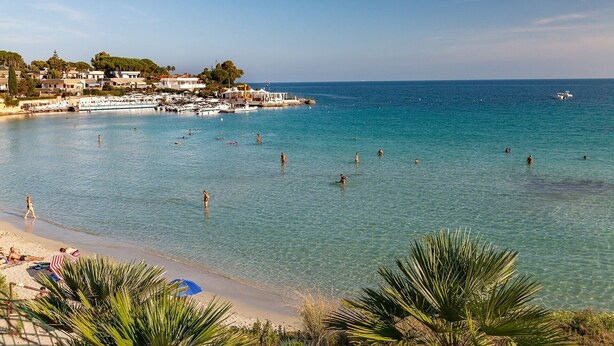 A coastal beach scene with clear turquoise water, a sandy shore, and a marina with boats. - Villa San Tommaso - Four Bedroom Villa, Sleeps 8 (Syracuse)