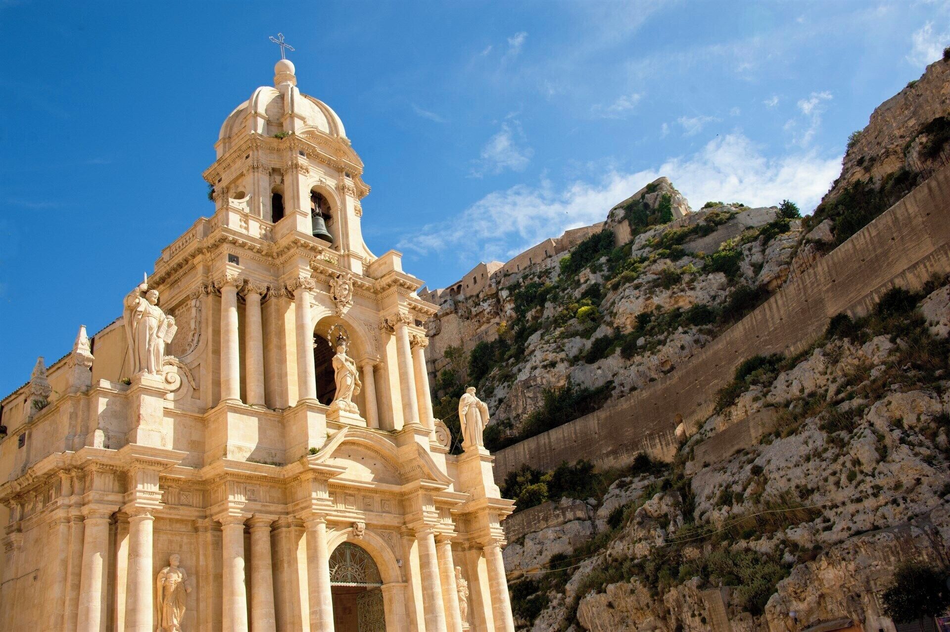 Une église historique, dotée d’un clocher et de statues, qui se dresse sur un arrière-plan montagneux.