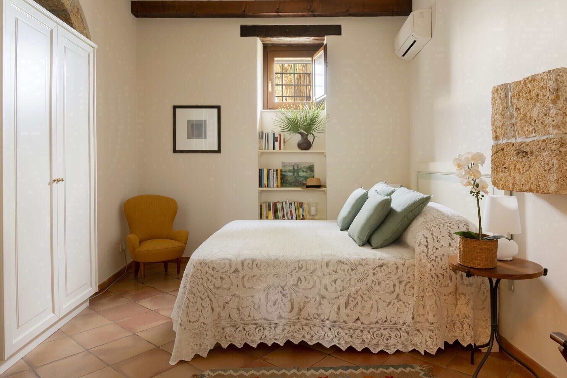 Un dormitorio con cama, una silla, una estantería y ventana.