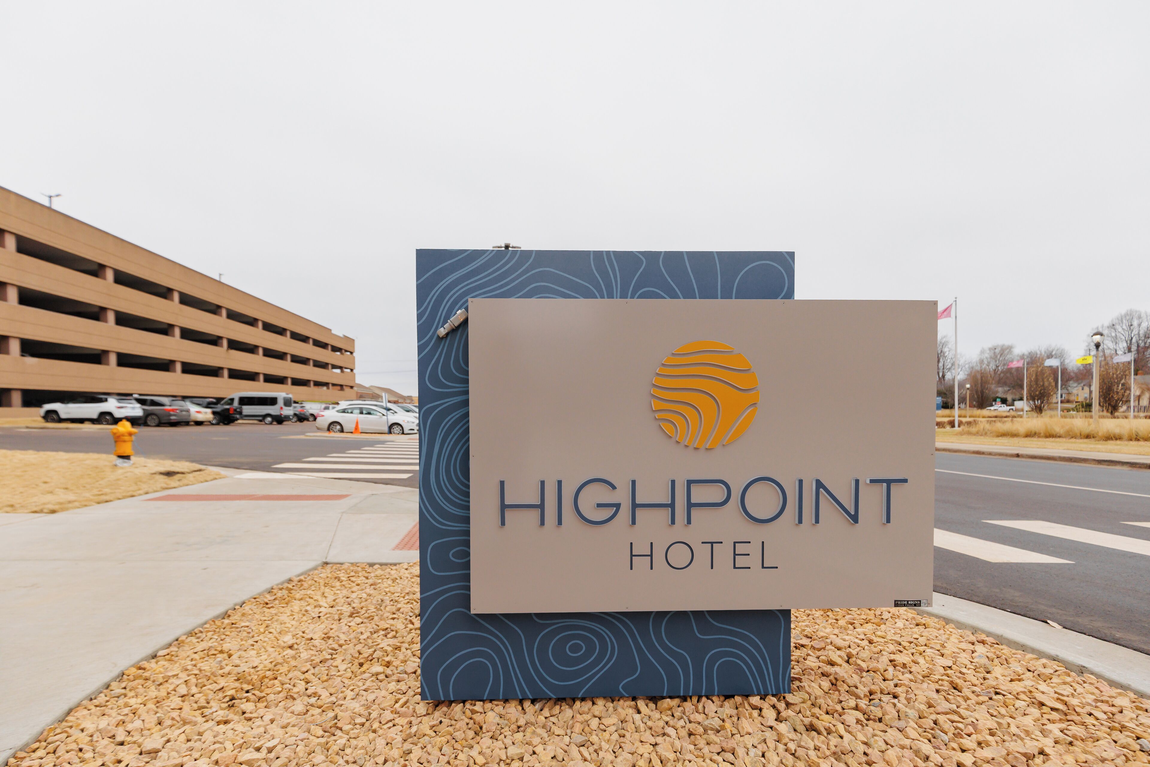 Une enseigne pour l’hôtel Highpoint, au design moderne, située à proximité d’un parking et d’une route.