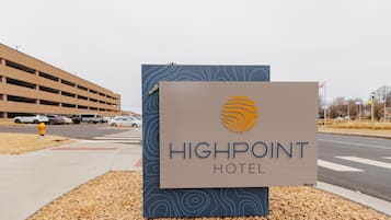 Une enseigne pour l’hôtel Highpoint, au design moderne, située à proximité d’un parking et d’une route.