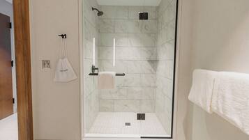 Een moderne douche met een glazen deur, marmeren tegels en een handdoekrek met een witte handdoek.
