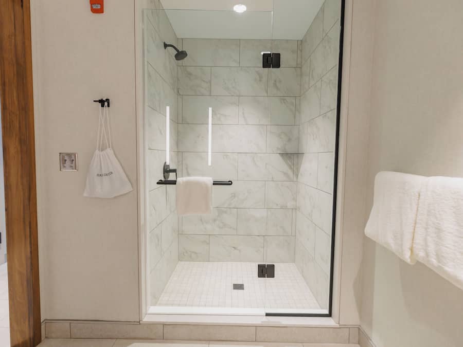 Een moderne douche met een glazen deur, marmeren tegels en een handdoekrek met een witte handdoek.