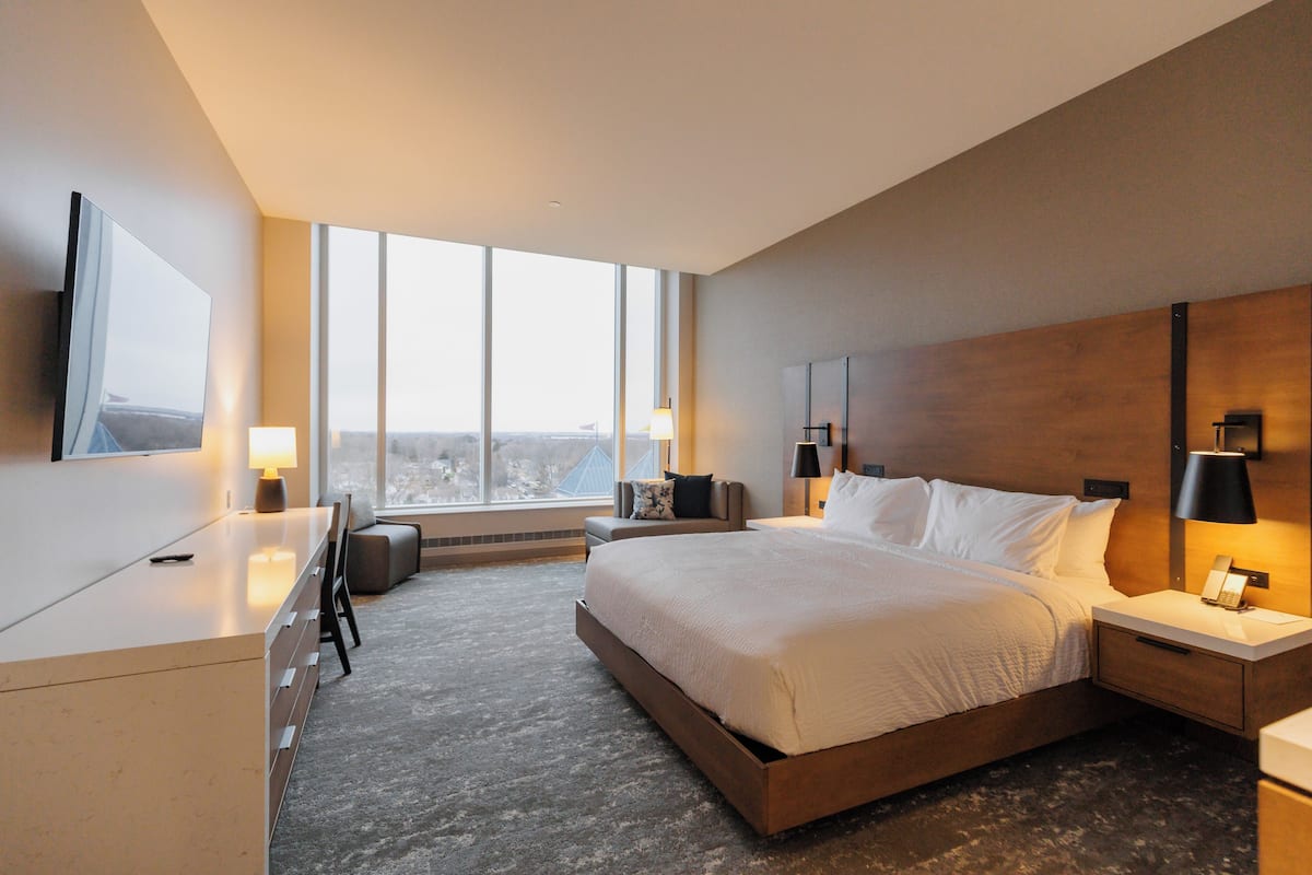 A modern hotel room with a large bed, a desk, and a view of the city.