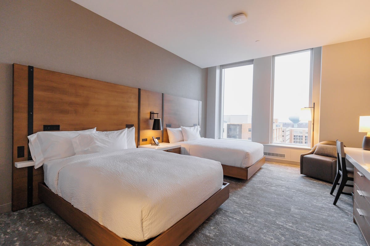 A hotel room with two beds, a desk, and a chair.
