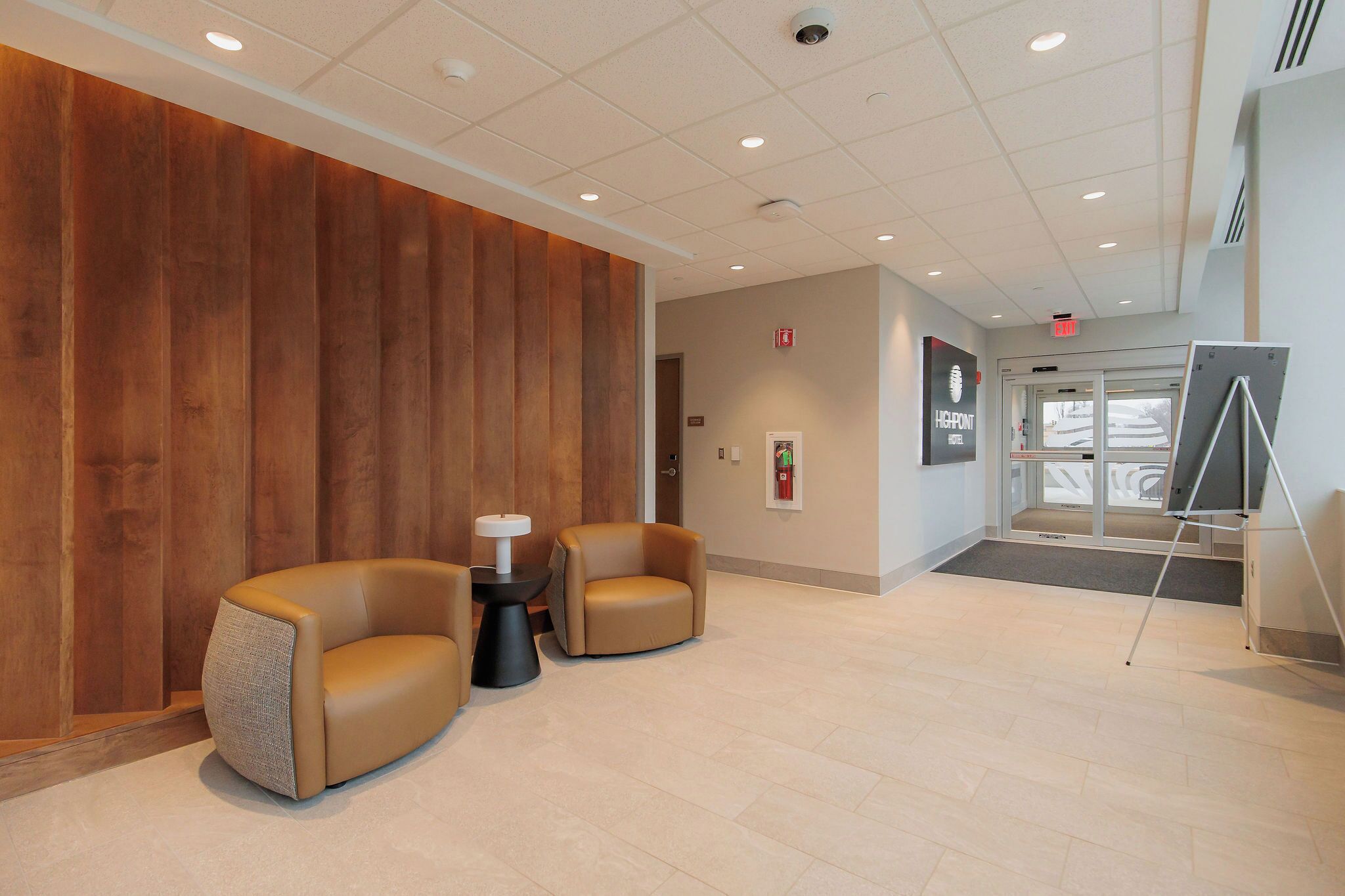 A lobby with two leather armchairs, a small table, and a large screen on a stand.