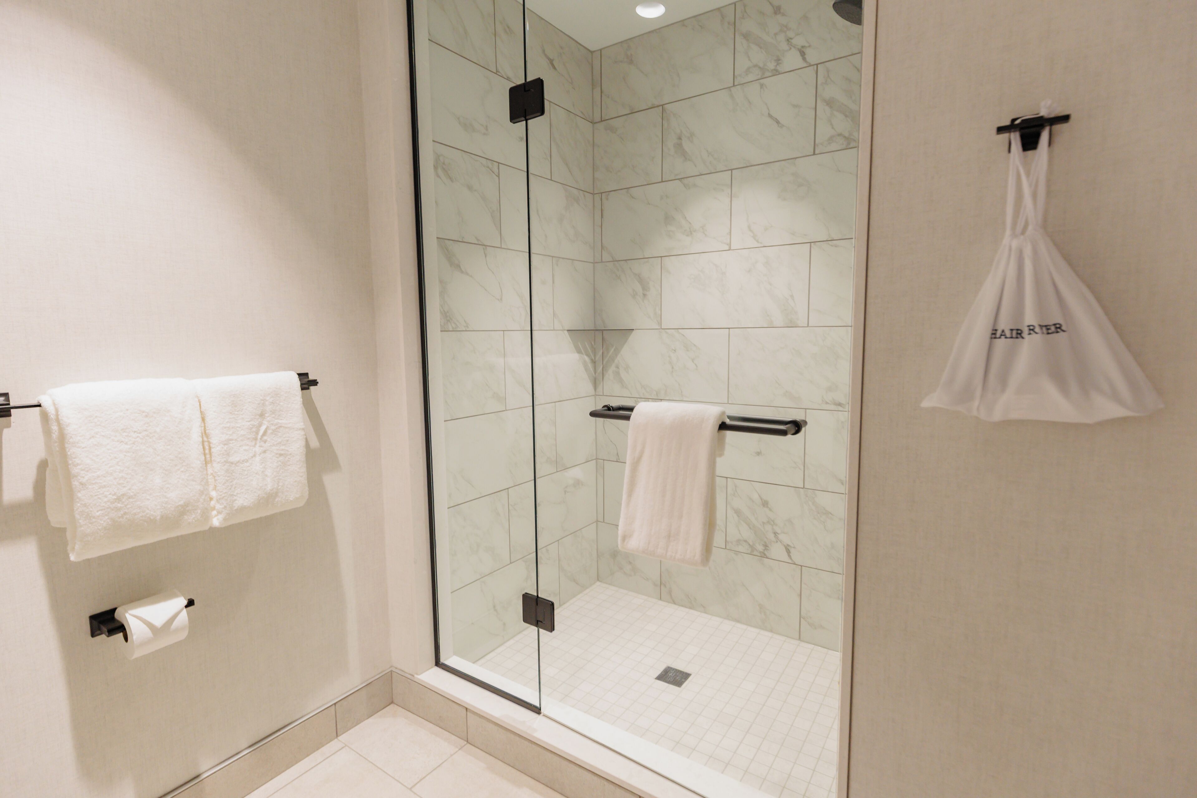 A modern bathroom with a glass-enclosed shower, marble tiles, and two white towels hanging on towel bars.