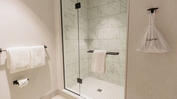 A modern bathroom with a glass-enclosed shower, marble tiles, and two white towels hanging on towel bars.