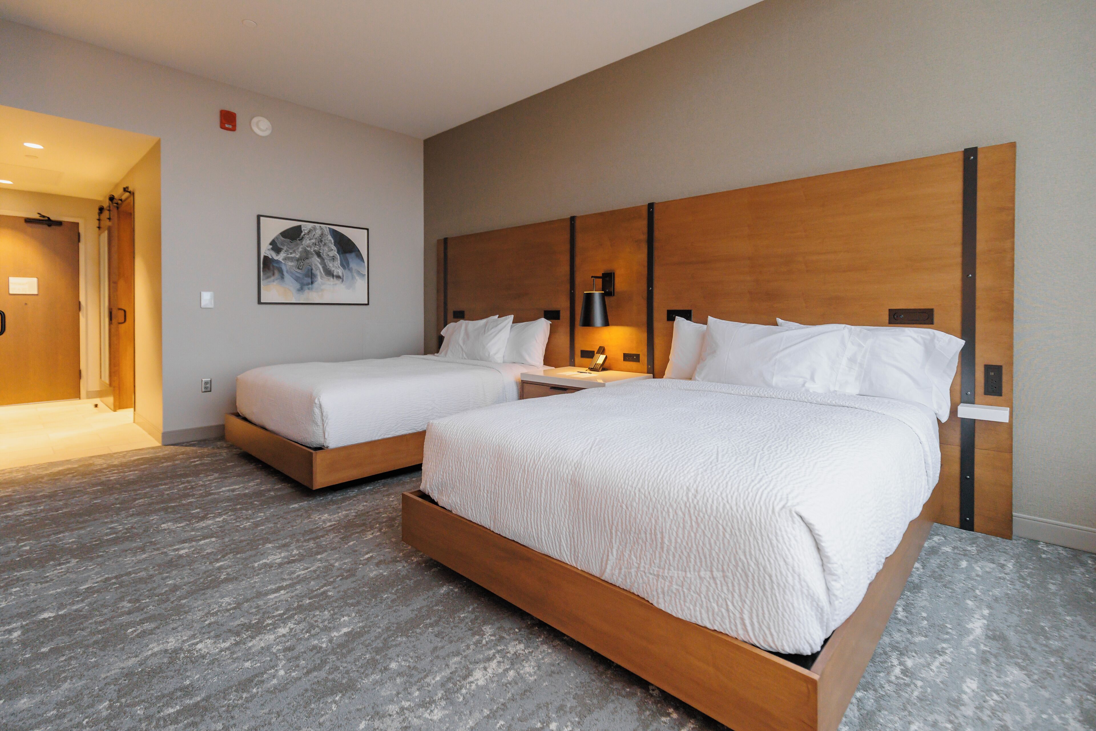 Een hotelkamer met twee bedden, een houten hoofdbord, een nachtkastje met een lamp en een lijst aan de muur.