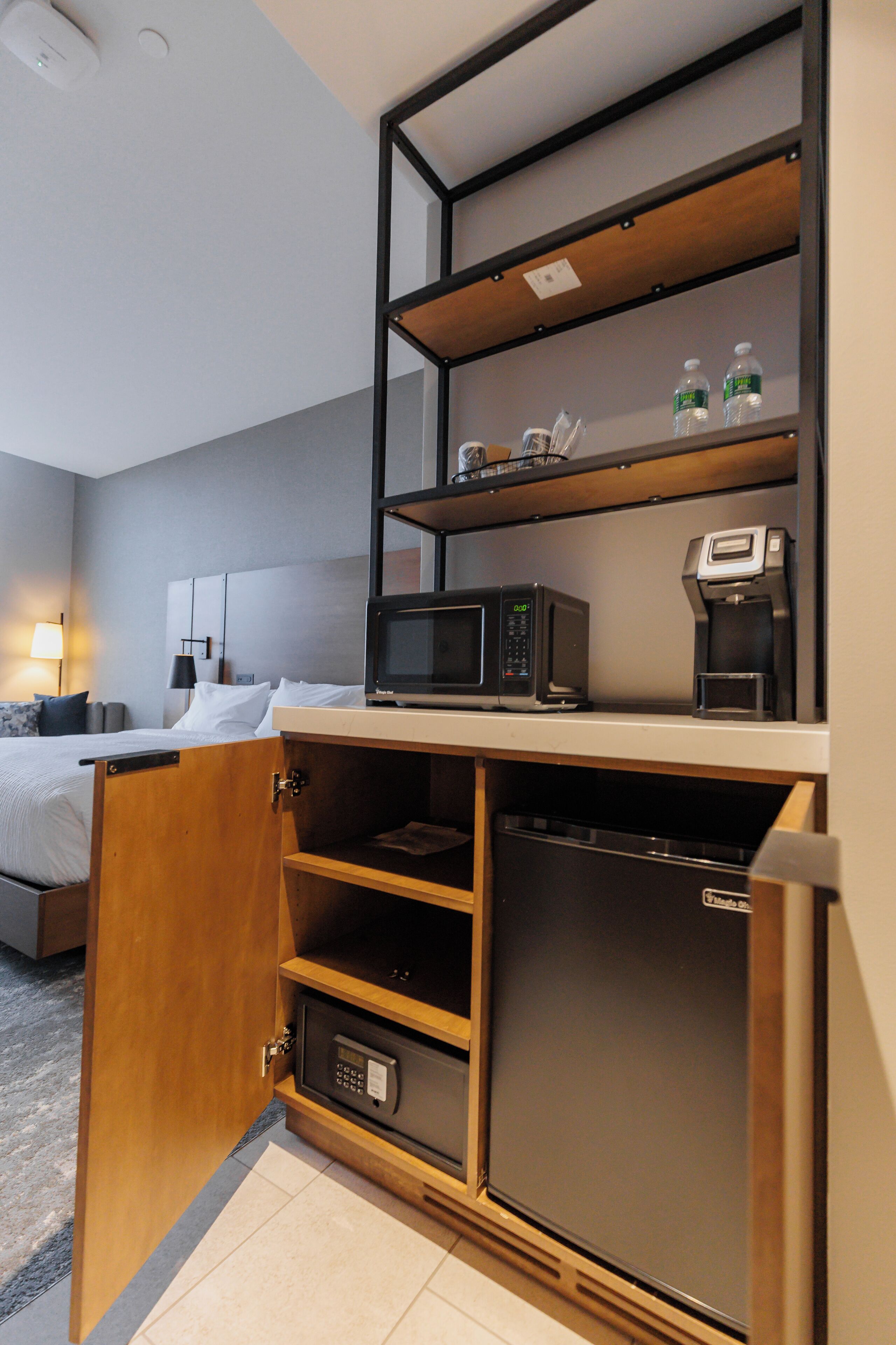 Une chambre d’hôtel de taille réduite, équipée d’un lit, d’un four à micro-ondes, d’une machine à café et d’un réfrigérateur.