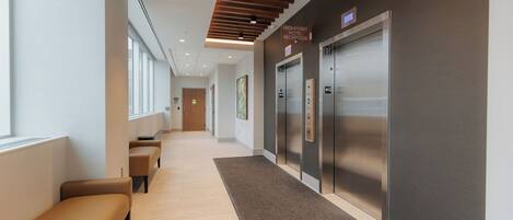 A hotel reception area with a long hallway, seating, and elevators.