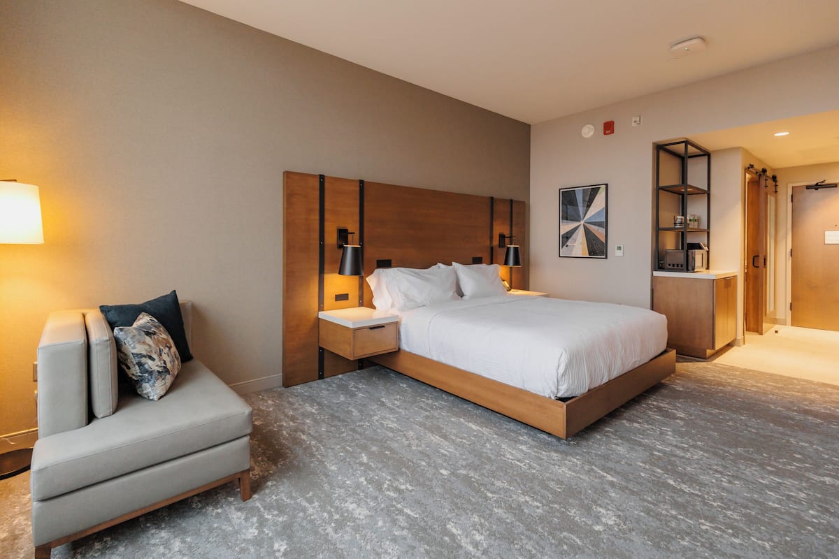 A modern hotel room with a large bed, a seating area, and a small desk.