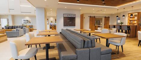 A modern restaurant with high tables, cushioned seating, and a wooden ceiling.