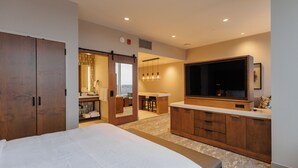 A hotel room with a large bed, wooden wardrobe, a TV, and a kitchenette area. - Highpoint Hotel (Sioux Falls)