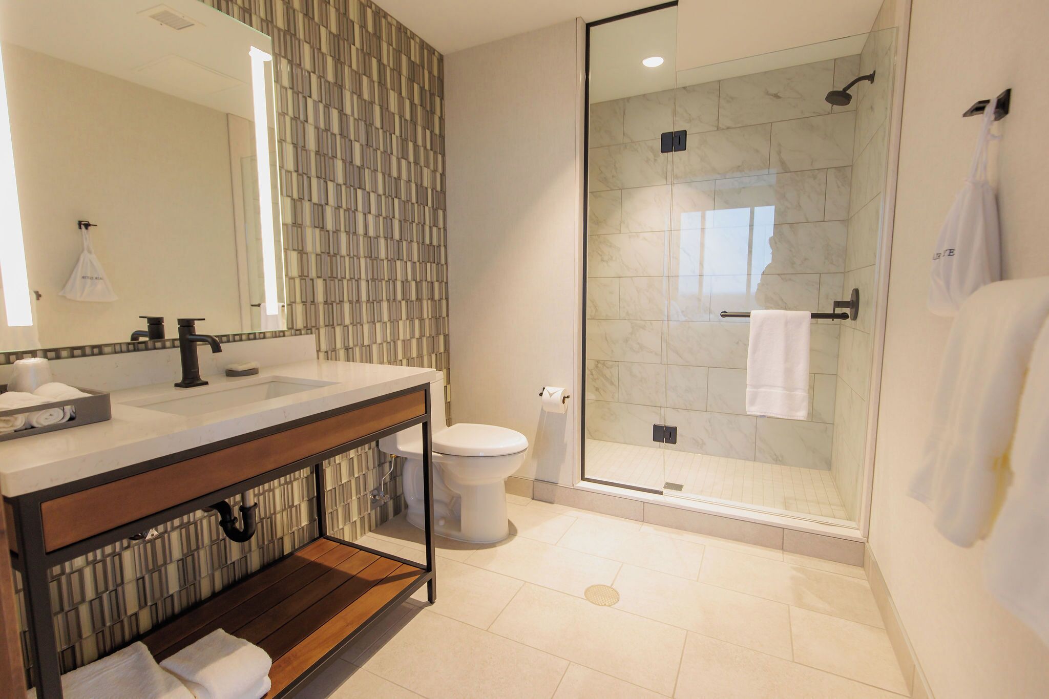 A modern bathroom with a glass-enclosed shower, a large mirror, and a wooden vanity.