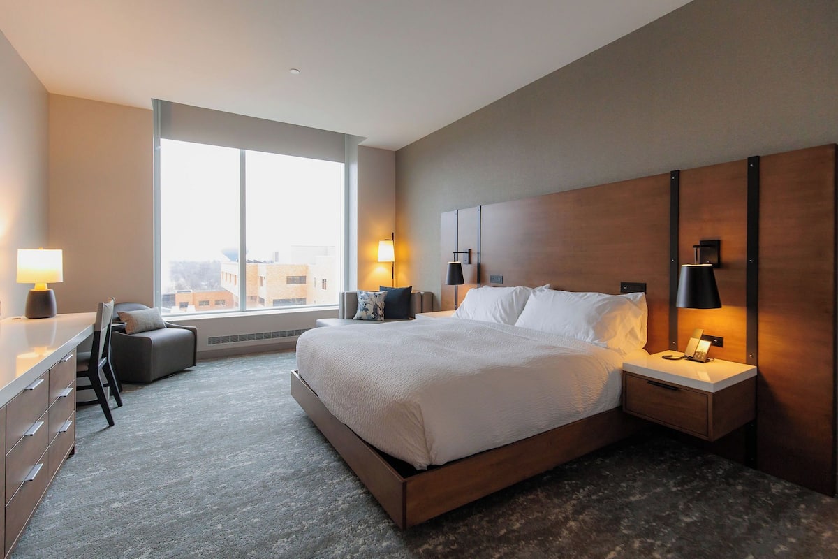 A modern hotel room with a large bed, bedside tables, a desk, and a chair.