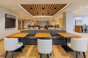 Um restaurante moderno com área de estar central, mesas de madeira e cadeiras brancas.