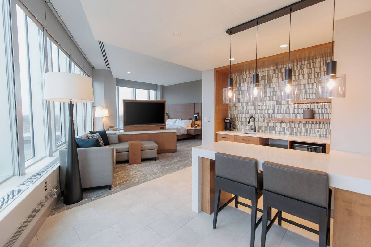 A modern living room with a sofa, a TV, and a kitchen area with a bar and pendant lights.