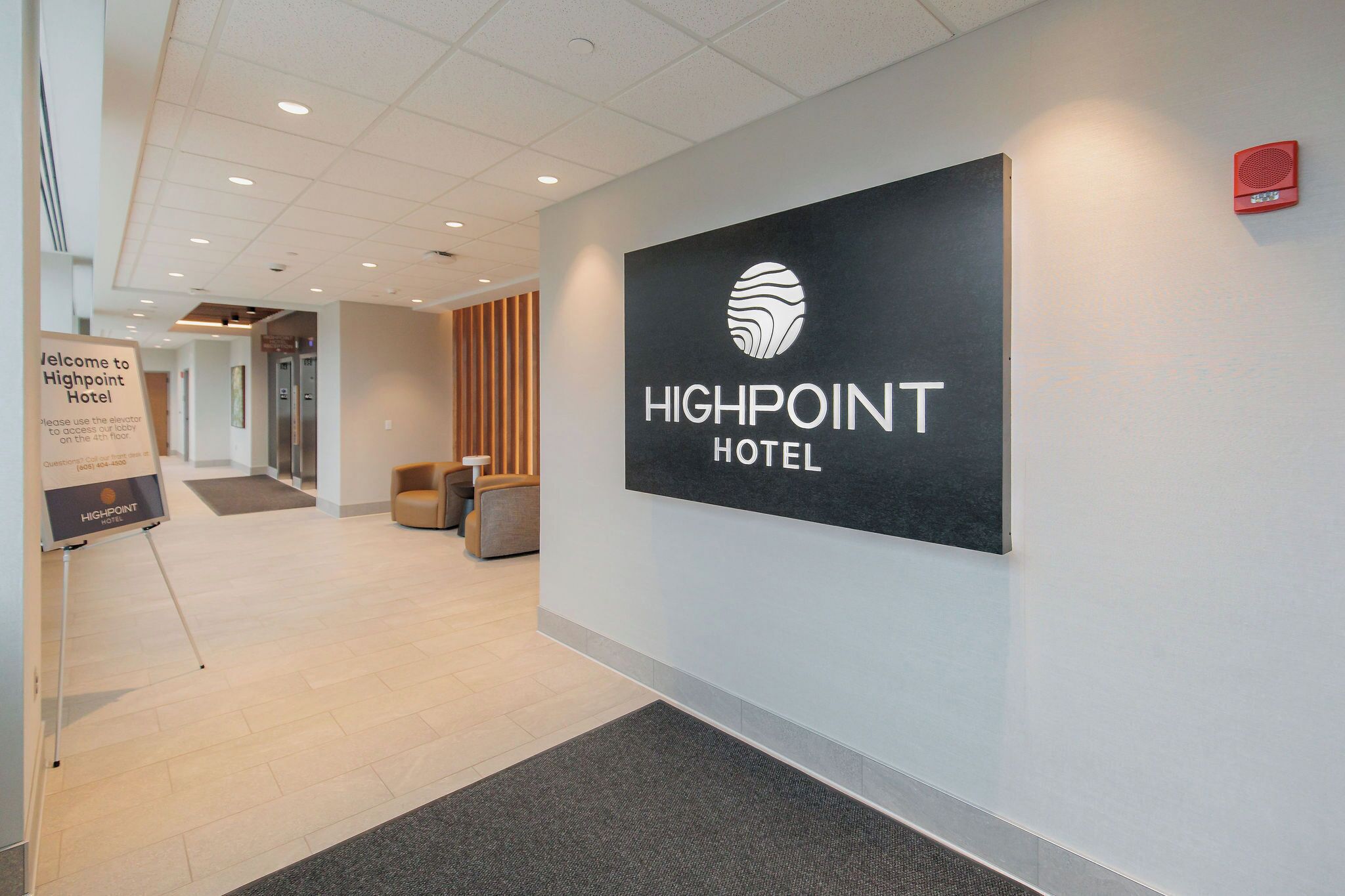 Uma área de recepção com um letreiro para Highpoint Hotel, um balcão de atendimento, uma sala de espera com cadeiras e um elevador ao fundo.