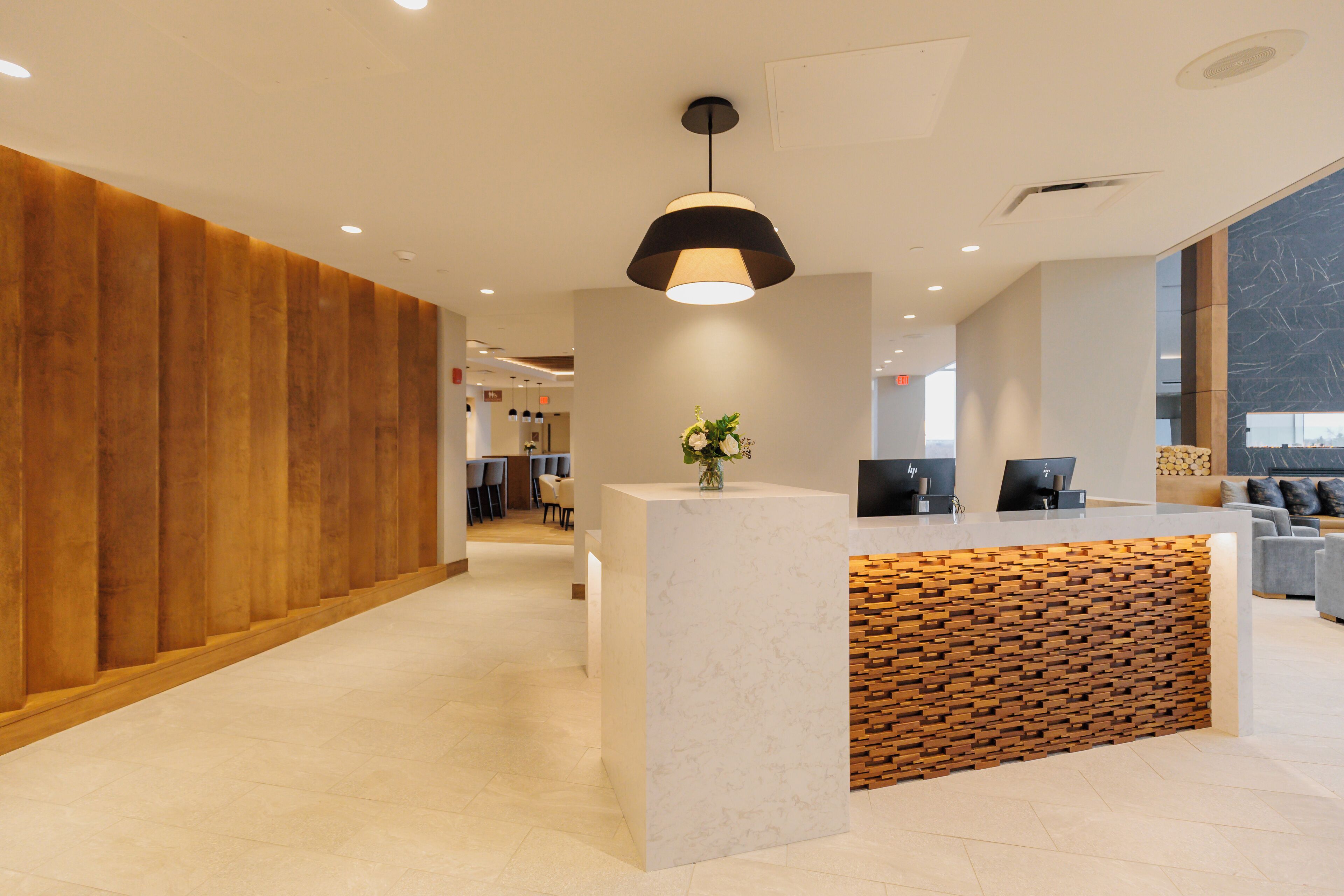 Una moderna zona de recepción con un panel de madera decorativo, un mostrador de mármol y un amplio ventanal que proporciona luz natural.