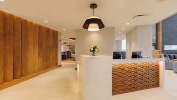 Una moderna zona de recepción con un panel de madera decorativo, un mostrador de mármol y un amplio ventanal que proporciona luz natural.