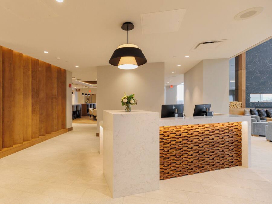Una moderna zona de recepción con un panel de madera decorativo, un mostrador de mármol y un amplio ventanal que proporciona luz natural.