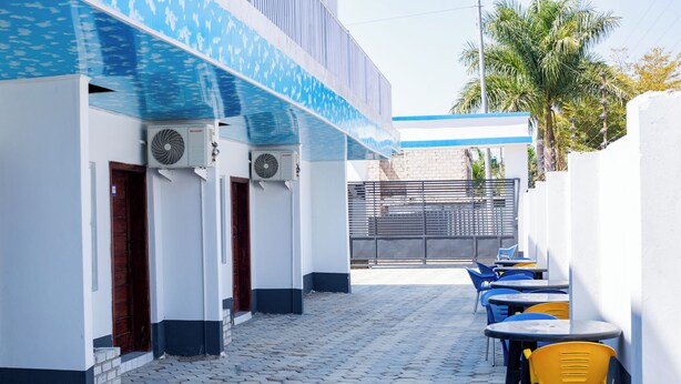 Un patio con pavimento de piedra hexagonal, mobiliario exterior con sillas amarillas y azules, y unidades de aire acondicionado en la fachada del edificio.