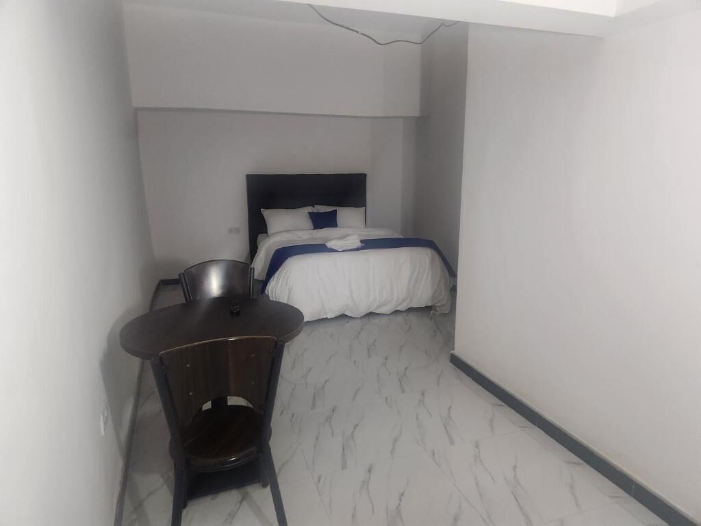 Une petite chambre d’hôtel étroite, avec un lit simple, une table de chevet et une chaise.