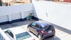 Dos coches estacionados en un área cubierta para estacionamiento, con una pared blanca y una planta en maceta.