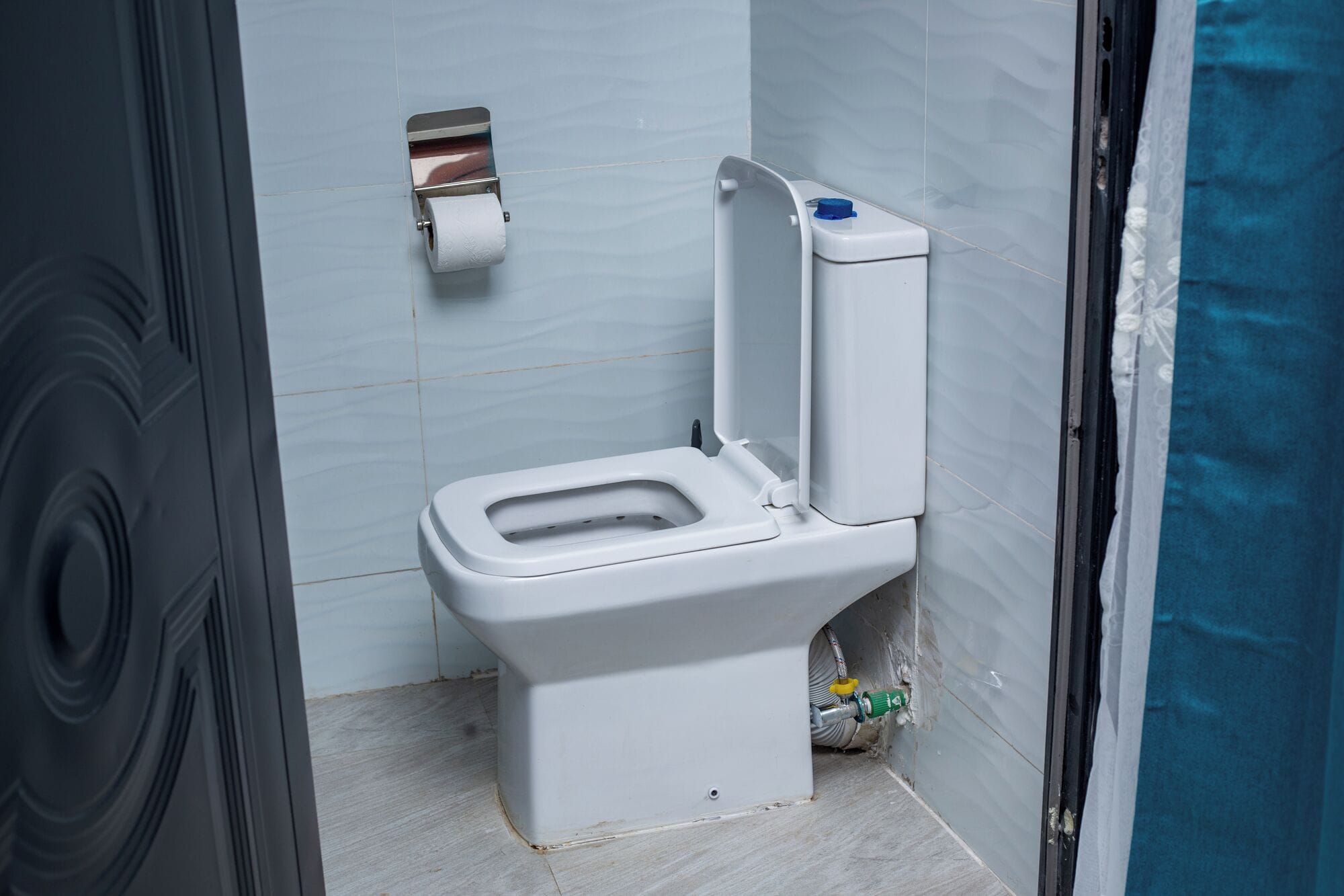 A toilet in a bathroom with a toilet paper holder on the wall.
