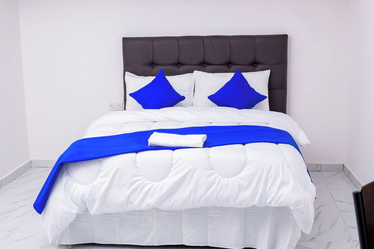 A bed with a dark headboard, white bedding, and blue accents.