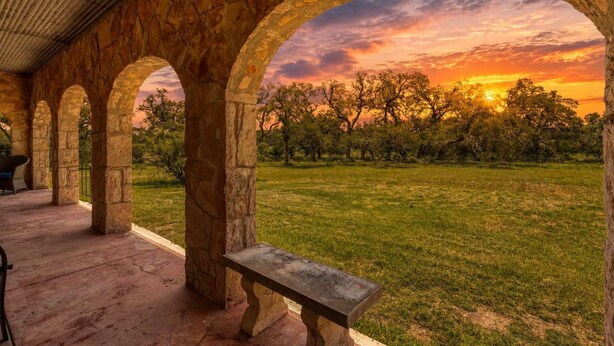 A stone archway structure with a bench, overlooking a grassy field with trees and a sunset view. - Peaceful 3-Bedroom Ranch Retreat Near Blanco (Blanco)