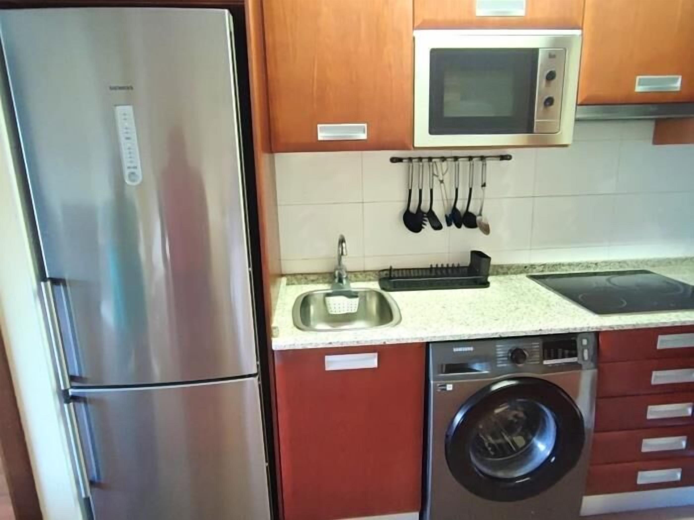 Een kleine keuken met een roestvrijstalen koelkast, een magnetron, een spoelbak en een ingebouwde wasmachine.