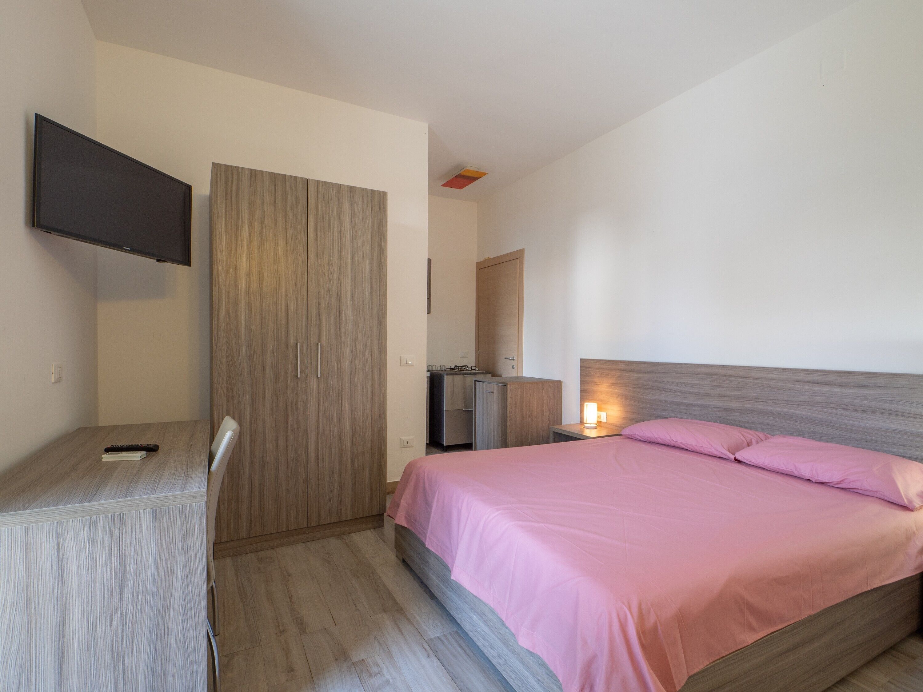 Een slaapkamer met een bed, nachtkastje, televisie, bureau en kledingkast.