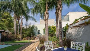 Una veranda con sedie bianche e un tavolo, circondata da palme e un giardino.