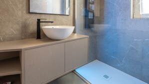 Un bagno moderno con un lavabo bianco a forma di vaso, un rubinetto nero, uno specchio sopra il lavabo e una doccia con porta in vetro.