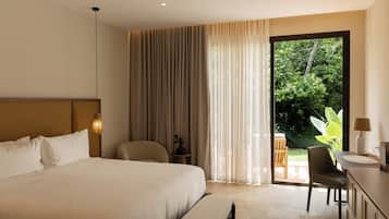 A hotel room with a large bed, a desk, a chair, a small table, and a view of greenery outside.